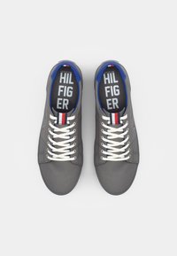 Gray canvas sneakers with white laces, blue interior, and a small red and white accent near the laces. "TOMMY HILFIGER" printed on insoles.