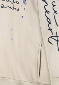 Hellbeiges Sweatshirt mit marineblauer Stickerei und blauen Paillettenakzenten. Verfügt über eine Fronttasche und gerippte Bündchen. Glatte Textur, lockere Passform.