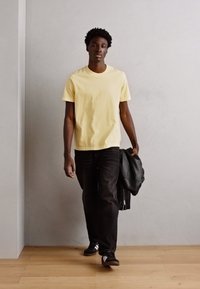Yellow cotton T-shirt with short sleeves, paired with black jeans and black sneakers. A black leather jacket is draped over one arm.
