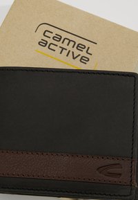 Portefeuille en cuir noir avec une bande texturée marron, présentant des détails de couture. La boîte en arrière-plan affiche le logo "camel active".