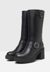 Bottes noires en cuir montantes avec un talon épais, dotées d'un détail de boucle sur le côté et d'une texture mate lisse. Semelle en caoutchouc pour une meilleure adhérence.