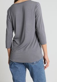 Graues Langarmshirt mit rundem Ausschnitt und weicher Textur. Getragen zu hellblauen, locker sitzenden Jeans. Einfaches, lässiges Design.