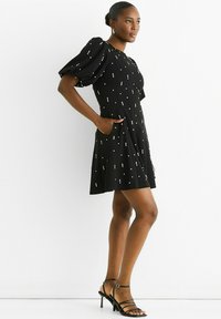 Black dress with puff sleeves, featuring scattered metallic accents. Smooth fabric with pockets and A-line shape, paired with strappy black heels.