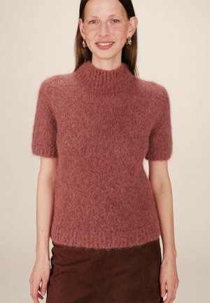 Pull à col montant, à manches courtes, en tissu rose doux et duveteux, avec une coupe décontractée, présentant des bords côtelés autour du col et de l'ourlet.