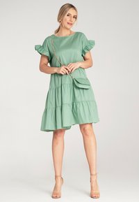Jasnozielona, warstwowa sukienka z krótkimi falbankowymi rękawami, wykonana z gładkiego materiału. W zestawie mała, dopasowana torebka na ramię.