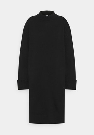 Schwarzes Strickkleid mit langen Ärmeln, einem gerippten Stehkragen und breiten gerippten Bündchen auf einfarbigem Hintergrund.