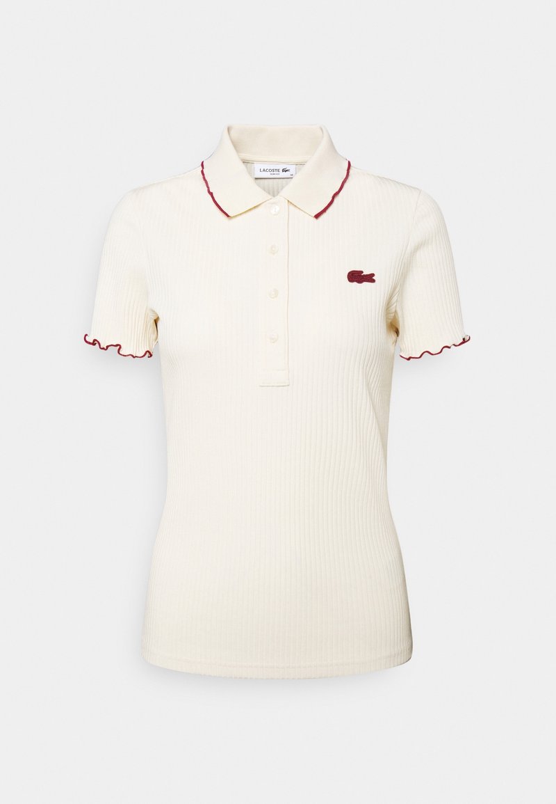 Polo côtelé à manches courtes couleur crème avec patte de boutonnage, finition rouge au col et aux manches, et logo rouge brodé sur la poitrine.