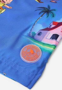 Mėlyni maudymosi šortai su animaciniu piešiniu, kuriame vaizduojami palmiai ir namas, papuošti oranžiniu apvaliu logotipo antpletu prie krašto.