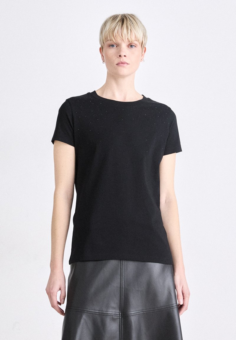 Melnā, īsām piedurknēm t-krekls ar apaļu kakla izgriezumu, ar smalkiem rotājumiem uz pleciem. Izgatavots no mīksta kokvilnas auduma.