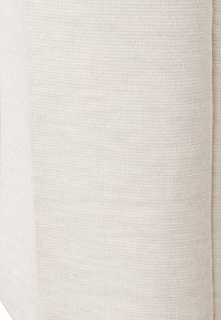 Tejido beige claro con un patrón texturizado de punto y acentos suaves. El material parece suave y ligeramente elástico.
