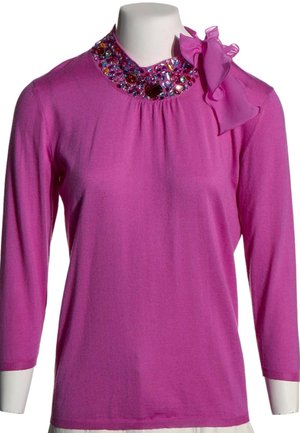 Haut à manches longues fuchsia avec encolure ornée de bijoux et grand nœud en tissu sur l'épaule gauche, présenté sur un mannequin blanc.