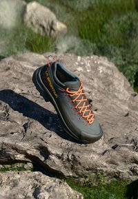 Šedá venkovní obuv s oranžovými tkaničkami, s texturovaným povrchem a odolnou gumovou podrážkou. Viditelné logo značky "La Sportiva".