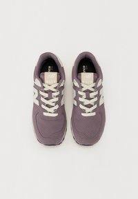 Lilla semskede sneakers med nettingpaneler, hvite lisser og en fremtredende "N"-logo på sidene. Polstret såle og svart gummisåle.