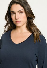 Námořnický modrý v-neck top s dlouhým rukávem vyrobený z měkkého materiálu. Má jednoduchou, hladkou texturu s uvolněným střihem a jemným švem.