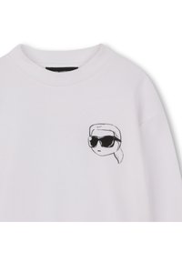 Λευκό φούτερ με μια μικρή μαύρη ζωγραφιά ενός ατόμου με γυαλιά ηλίου και κοτσίδα στο αριστερό μέρος του στήθους. Βαμβακερό υ λικό.