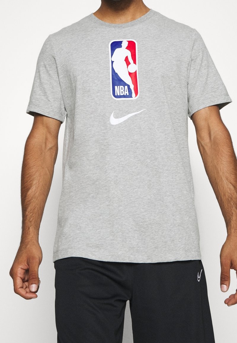 Szara bawełniana koszulka z krótkim rękawem z dużym logo NBA w niebieskim i czerwonym kolorze, z białym logo Nike na piersi. Okrągły dekolt.