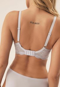 Jasnoszary koronkowy biustonosz z regulowanymi ramiączkami, z zapięciem na haftkę i delikatnym wykończeniem w kształcie falbany, połączony z gładkimi, dopasowanymi majtkami.