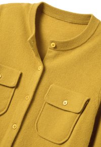 Maglione giallo lavorato a maglia con collo rotondo, dotato di due tasche frontali e chiusure con bottoni. Texture morbida con collo a coste e dettagli con bottoni.