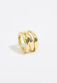 Anello triple band placcato in oro con una finitura liscia e lucida, caratterizzato da forme circolari intrecciate e una superficie interna testurizzata.