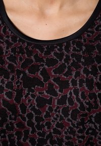 Top de punto negro con un patrón abstracto en burdeos y gris. Cuello redondeado con un ribete negro en contraste. Textura suave.