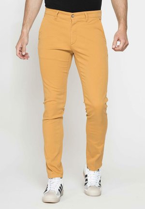 Pantalons en coton slim, couleur jaune moutarde, avec fermeture éclair et bouton argenté, dotés de poches latérales et d'une texture lisse et propre.