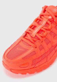 Nike bėgimo bateliai ryškiai oranžinės spalvos, su tinklinėmis detalėmis ir tekstūruotu apdovanojimu. Šniūreliai ir akcentai atitinka ryškią spalvų schemą.