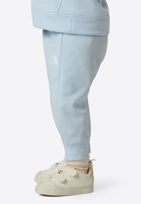 Light blue jogger pants made of soft fabric, featuring an elastic waistband and logo detail. Paired with cream sneakers with Velcro straps.