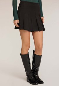 Zwarte geplooide rok met een gladde textuur, gecombineerd met zwarte laarzen tot de knie van leer. De rok heeft een getailleerde pasvorm en valt tot halverwege het bovenbeen.