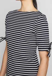 Top de manga corta a rayas en azul marino y blanco, con cuello redondo y puños atados, fabricado en una suave y elástica tela.