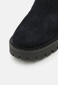 Black suede ankle boot with a chunky black rubber sole, featuring a textured tread and rounded toe design.