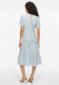 Robe bleu clair avec des manches courtes, motif floral, jupe à volants, détail en trou de clé au dos et texture de tissu lisse.