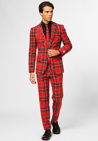Red plaid suit with a fitted silhouette, featuring black accents, buttoned blazer, and matching trousers. Black dress shoes complete the look.