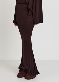 Brauner, figurbetonter langer Rock mit gerafftem Saum. Hergestellt aus dehnbarem Material. Kombiniert mit dunklen, klobigen Plateauschuhen.