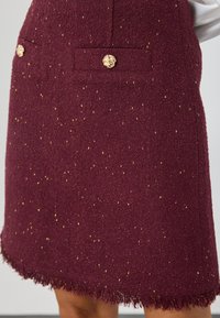 Burgundijas krāsas tvīda svārki ar izkliedētām zelta punktiņām, divām priekšējām kabatām ar zelta lauvu galvas pogām un saplēstu apakšmalu.