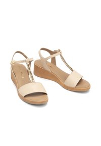 Beżowe sandały na koturnie z designem w kształcie litery T, z dodatkiem łańcucha. Gładka syntetyczna cholewka i teksturowana podeszwa zapewniająca przyczepność.