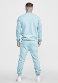 Světlomodrý svetr a kalhoty na cvičení, směs bavlny, žebrované manžety a pas, volný střih, čistý design, jednolitá textura, nošené s bílými teniskami.