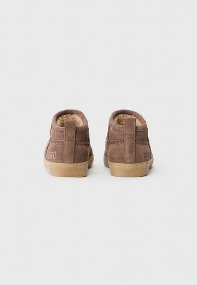 Brune semsko skinnstøvletter med mykt fleece-fôr, avrundet design og en lys tan gummisåle. Har en baksløyfe for enkel påkledning.