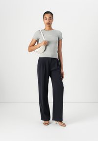 T-shirt grigio aderente con maniche corte, pantaloni neri a vita alta e una borsa a tracolla color crema. Sandali con tacco aperti completano il look.