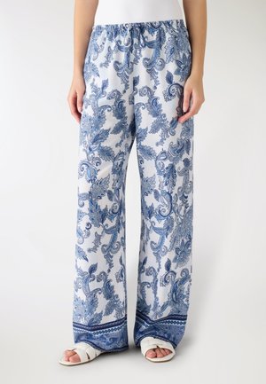 Pantaloni bianchi larghi con motivi floreali paisley blu, vita elasticizzata con coulisse, indossati con sandali bianchi aperti sulla punta su una persona.