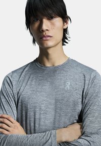 Grå langærmet sports-T-shirt med en meleret tekstur og et logo på øverste venstre bryst. Har rund hals og tætsiddende design.