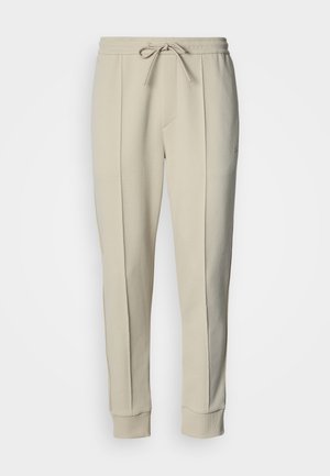 Beežid dressipüksid paelaga vöökohas, kitsenevate säärte ja küljetaskutega. Valmistatud pehmest puuvillasest segu kangast, millel on sile tekstuur.