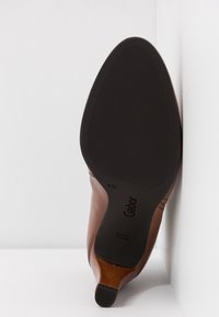 Chaussure en cuir marron avec un bout pointu et une semelle en caoutchouc noire. Elle possède une semelle texturée antidérapante et un logo embossé. Taille 4½.