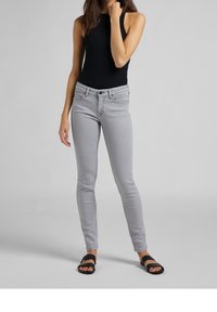 Top sin mangas negro con relieve, combinado con jeans ajustados gris claro y sandalias negras de tipo slide. El conjunto presenta una silueta ajustada y un diseño simple.