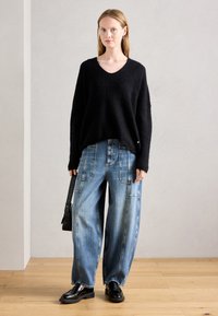Suéter negro de cuello en V y textura esponjosa, pantalones de mezclilla anchos de color azul claro con costuras visibles, zapatos de cuero negros y un pequeño bolso cruzado negro.