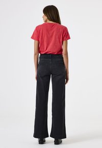 Schwarze weit geschnittene Jeans mit Gesäßtaschen, kombiniert mit einem roten strukturierten T-Shirt. Glattes Material mit lässiger Passform und gerader Silhouette.