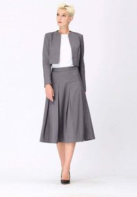 Veste grise ajustée avec un design court et une longue jupe plissée, tous deux en tissu léger. Porté avec un haut blanc et des talons noirs.