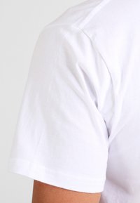 White cotton t-shirt with a crew neckline. Close-up of the short sleeve, highlighting the smooth texture and stitching details.