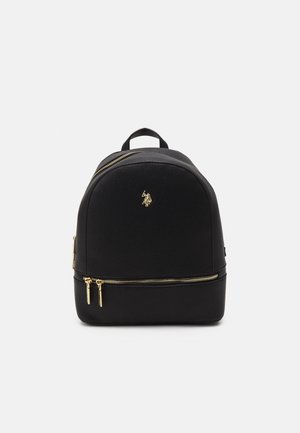 Pequeña mochila negra con asa superior, cremalleras doradas en los compartimentos delantero e inferior y un emblema de logo dorado en el centro delantero.