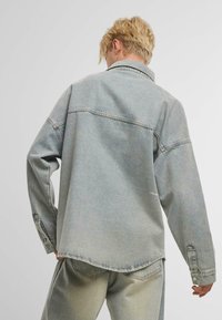 Hele hall hall denim jakk, millel on lõdva istuvus, terav kaelus ja nuppude mansetid. Sile tekstuur ja nähtavad õmbluse detailid.