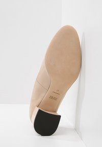 Scarpa con tacco alto nuda, con finitura lucida, punta affusolata e tacco in gomma nera. Texture liscia, cuciture laterali sottili e logo del marchio visibile.